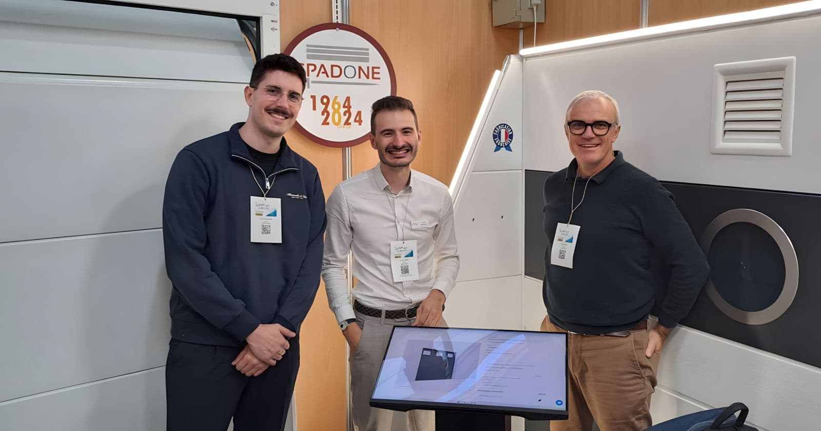 Joseph Spadone avec Simon Boddy et Benjamin Ducharne, cofondateurs de Simplyfirst, sur le stand Spadone devant un écran tactile qui présente le configurateur